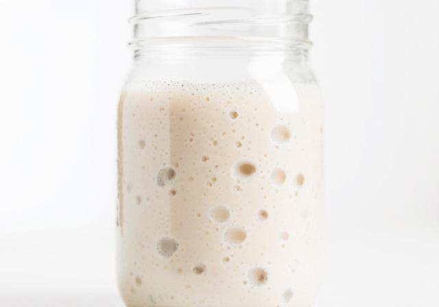 Frasco de cristal con masa madre burbujeante y activa al lado de ingredientes naturales