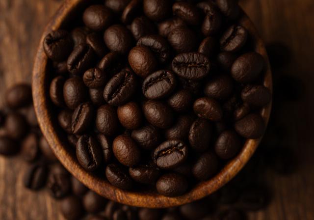 Granos de café recién tostados de color marrón intenso en un recipiente de madera